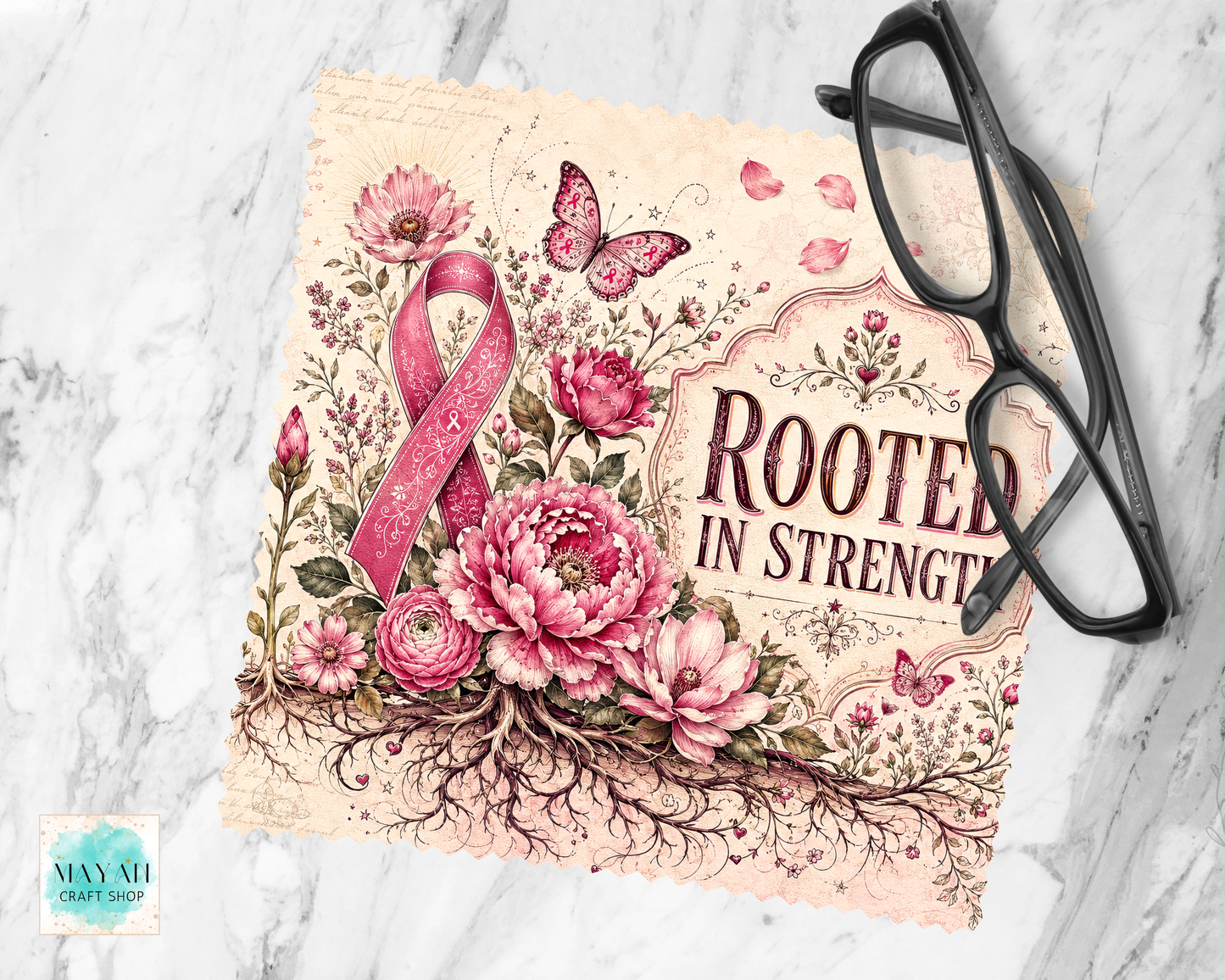 A lens cloth cleaner with the phrase “ROOTED IN STRENGTH” in dark lettering, surrounded by pink flowers, butterflies, and a pink awareness ribbon. The print is styled on a white marble surface with black eyeglasses placed on top.