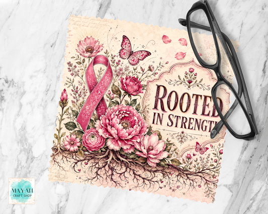 A lens cloth cleaner with the phrase “ROOTED IN STRENGTH” in dark lettering, surrounded by pink flowers, butterflies, and a pink awareness ribbon. The print is styled on a white marble surface with black eyeglasses placed on top.