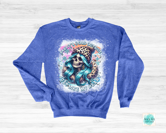 Blue sweatshirt with a graphic design of a skull with blue hair and leopard print elements on a white wooden background.