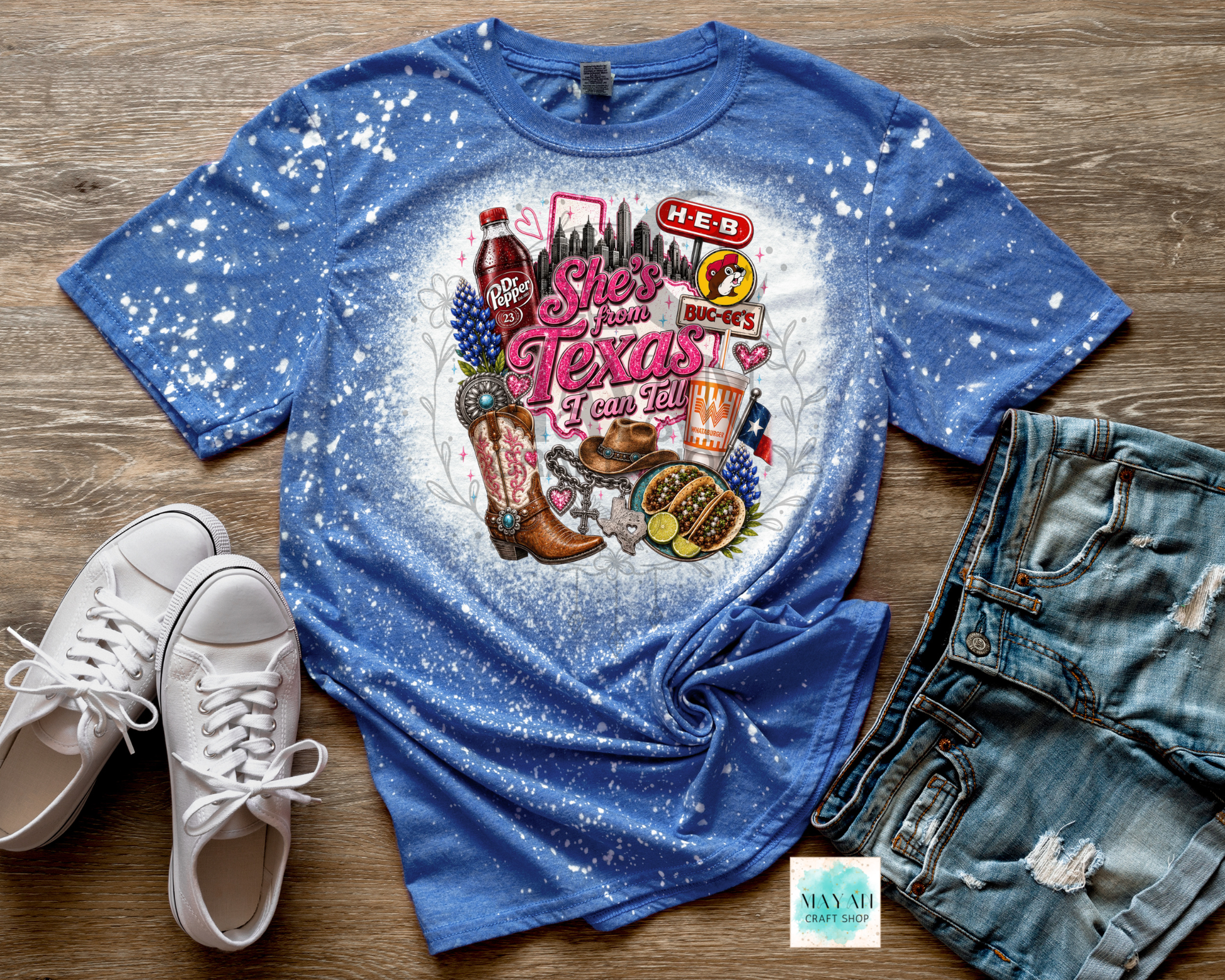 Blue t-shirt with Texas-themed graphics on a wooden surface with white sneakers and denim shorts.