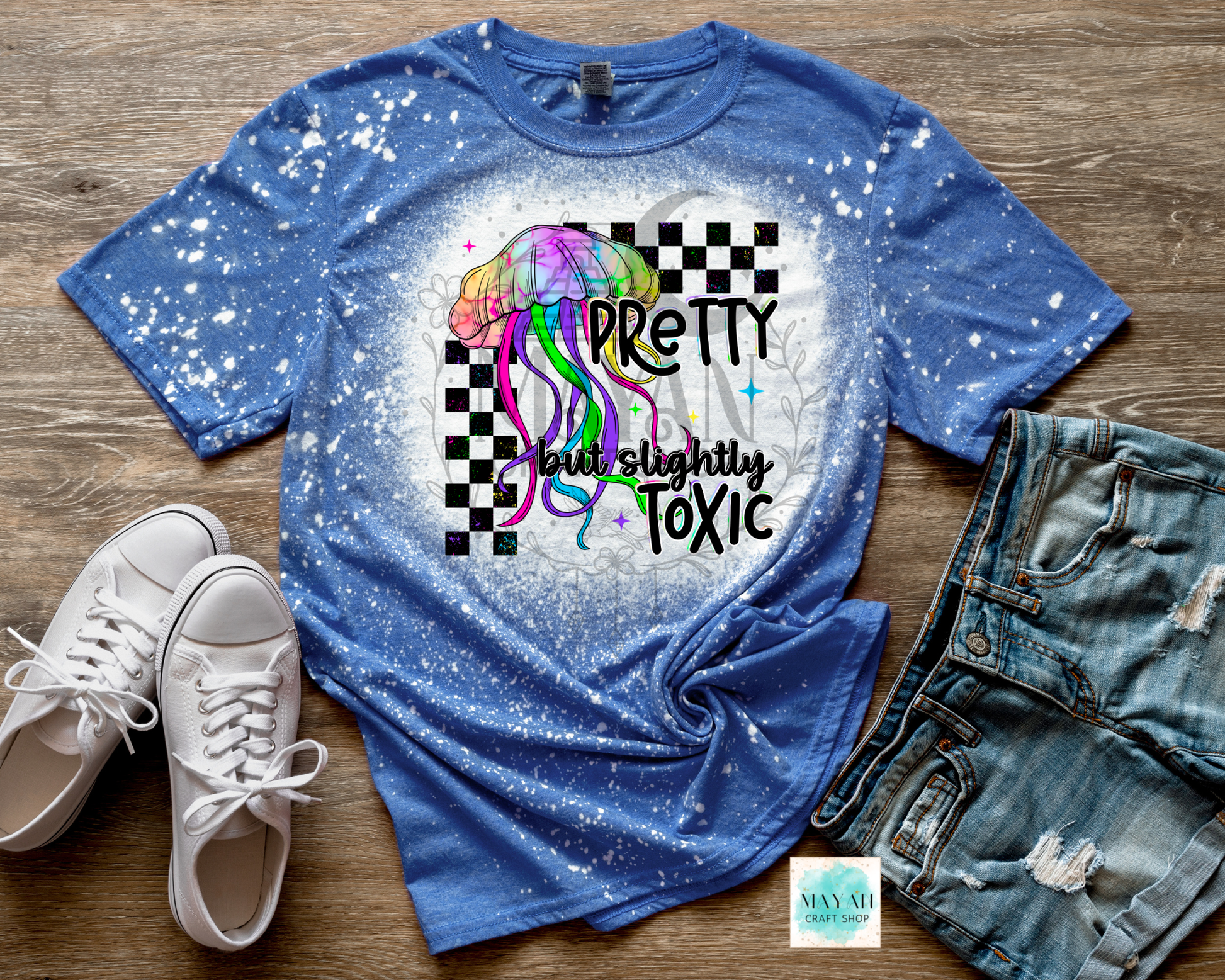 Blue t-shirt with colorful design and text on a wooden surface with shoes and shorts.