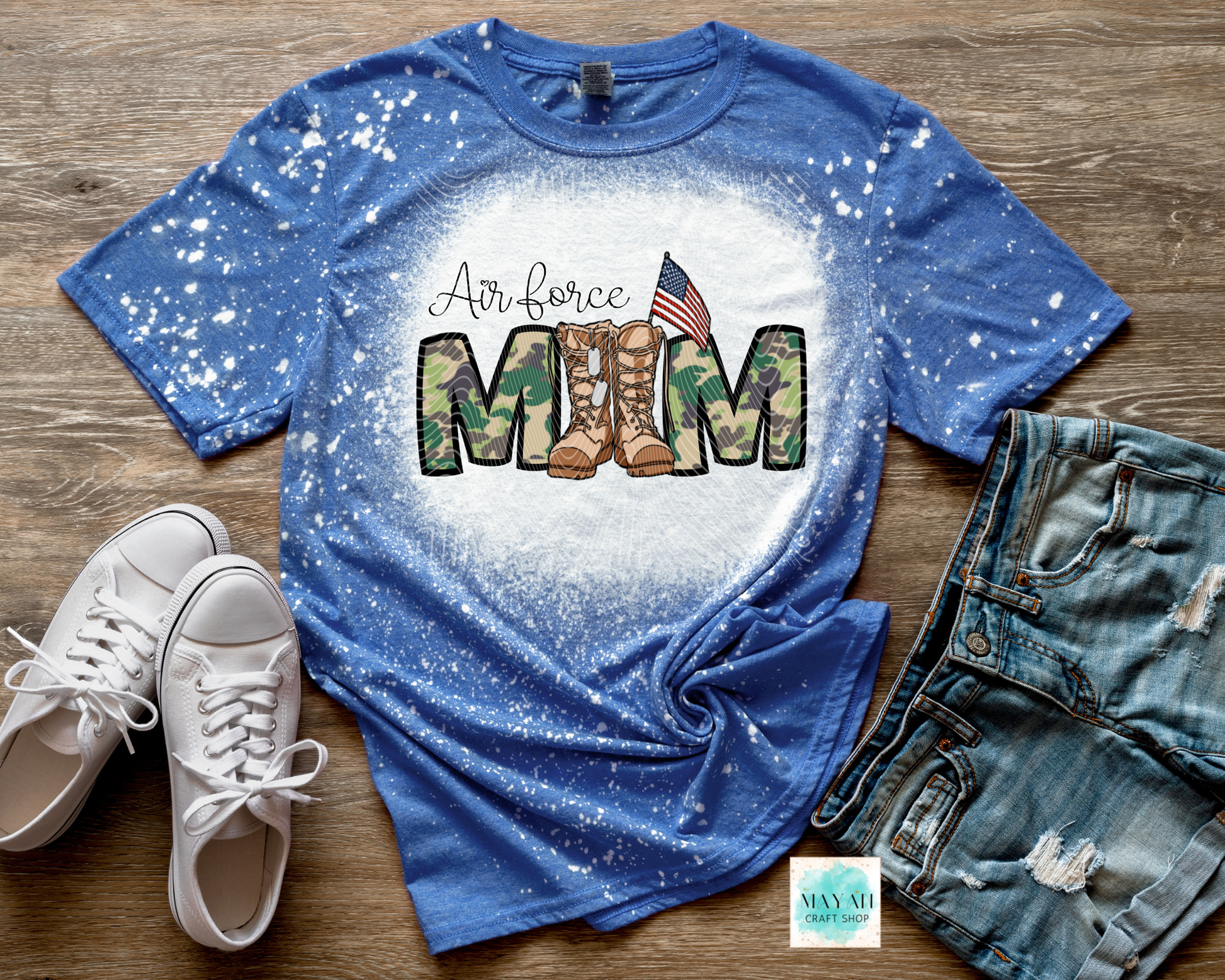 Blue t-shirt with military mom text and camouflage boots graphic on a wooden surface with white sneakers and jeans.