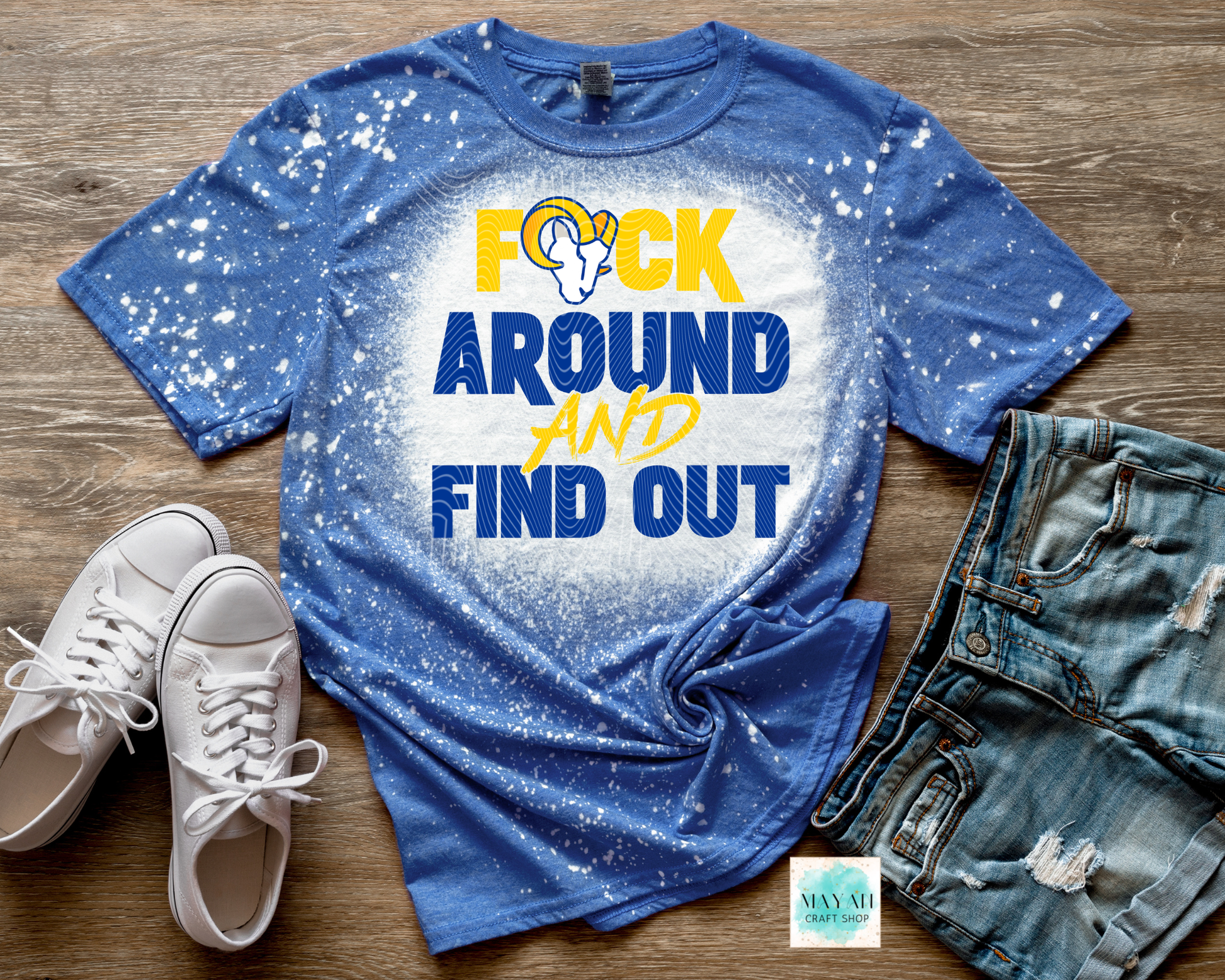 Blue t-shirt with graphic text, white sneakers, and denim shorts on a wooden surface