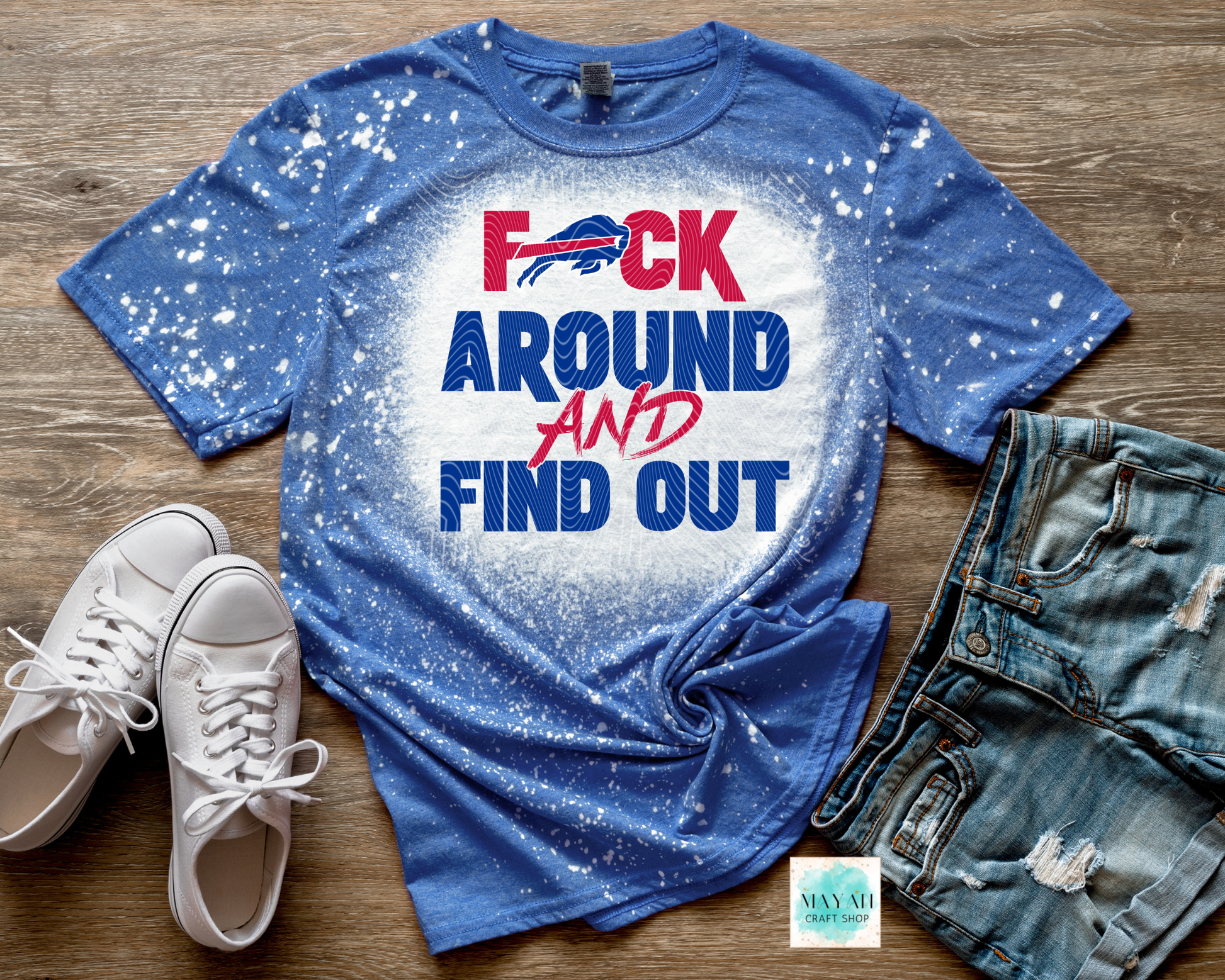 Blue t-shirt with graphic text on a wooden surface with shoes and jeans.