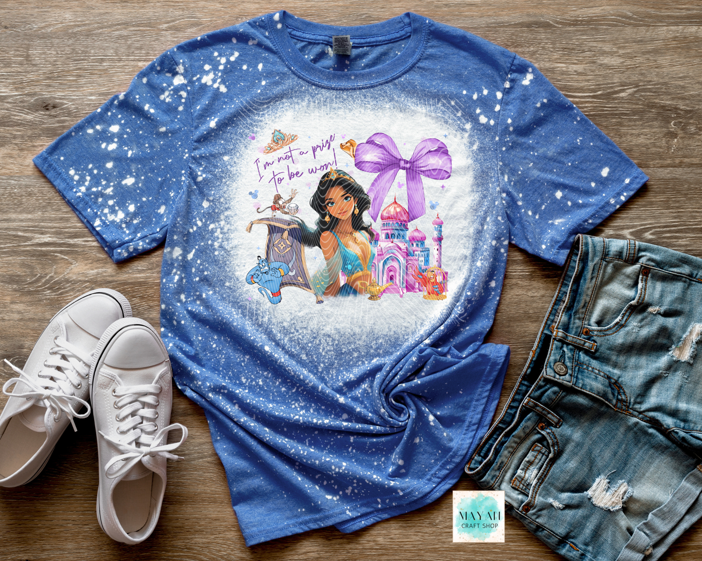 Blue t-shirt with princess graphic and text on a wooden surface with shoes and shorts.