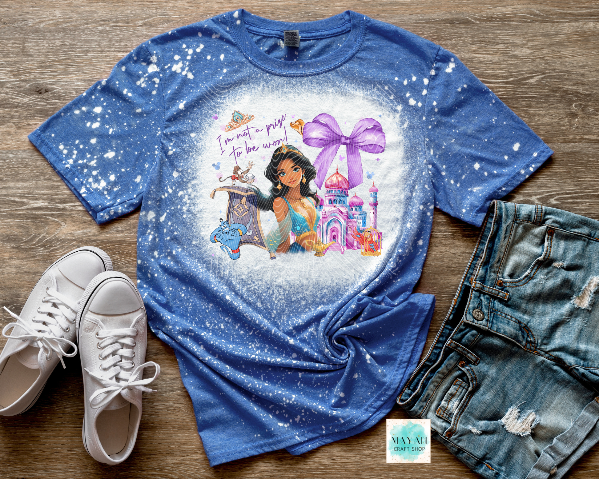 Blue t-shirt with princess graphic and text on a wooden surface with shoes and shorts.