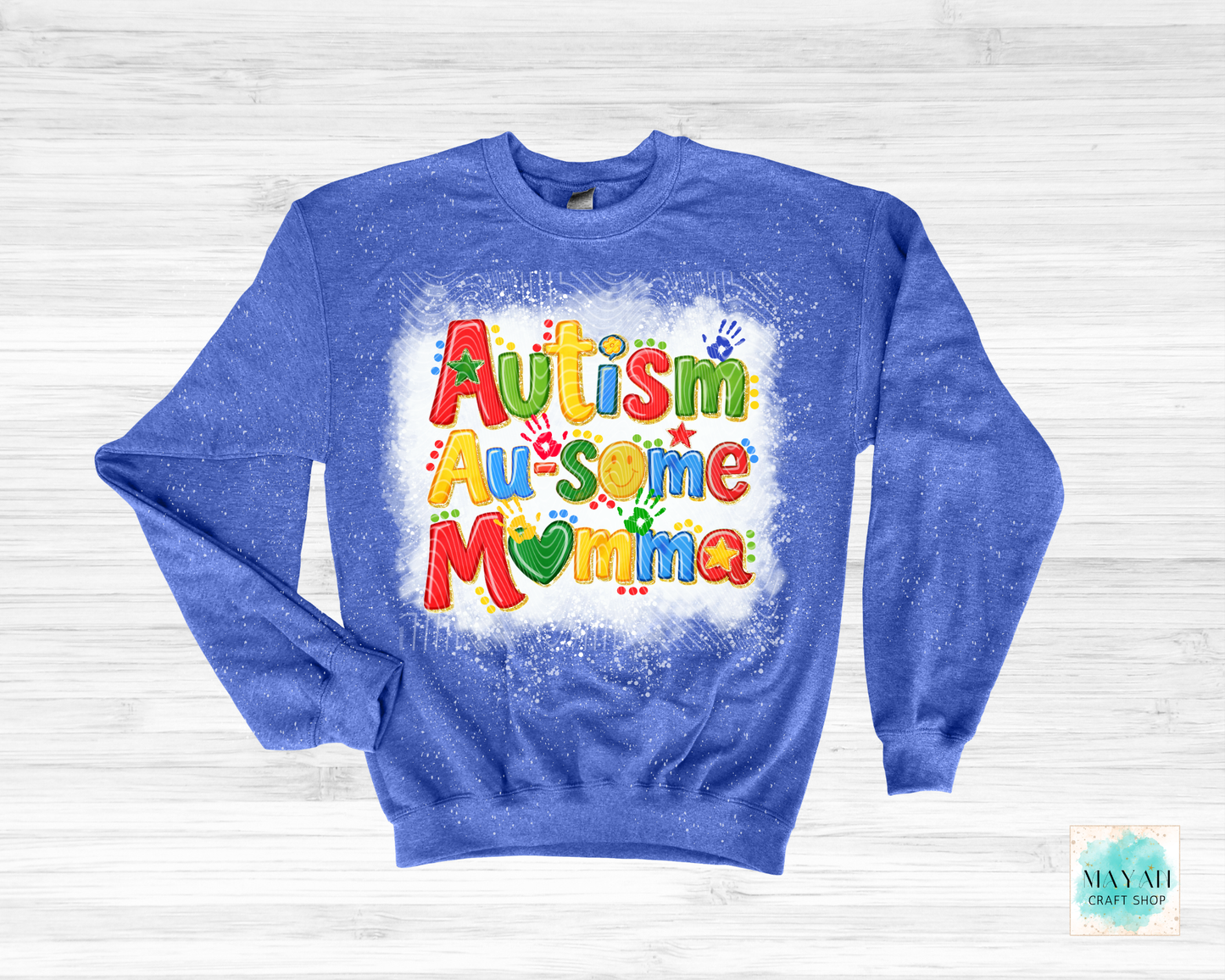 Blue sweatshirt with colorful 'Autism Awesome Momma' text on a white wooden background