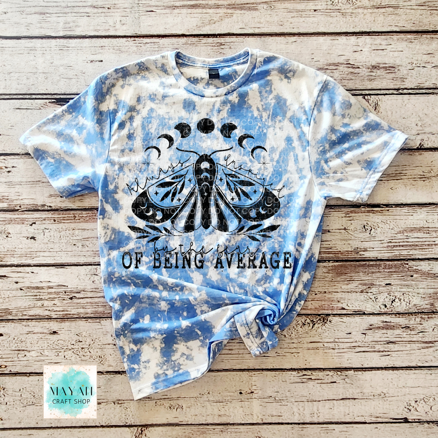 Tie-dye t-shirt with a black graphic and text on a wooden surface, featuring the brand 'Mayan Craft Shop'.