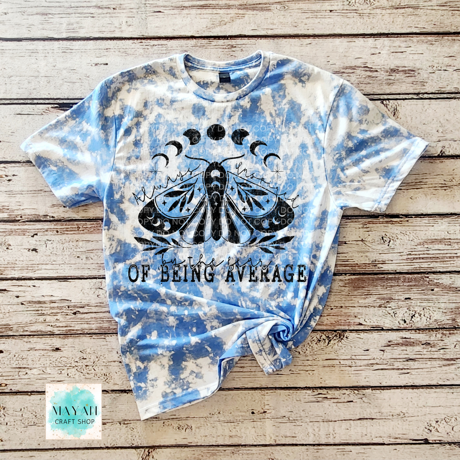 Tie-dye t-shirt with a black graphic and text on a wooden surface, featuring the brand 'Mayan Craft Shop'.