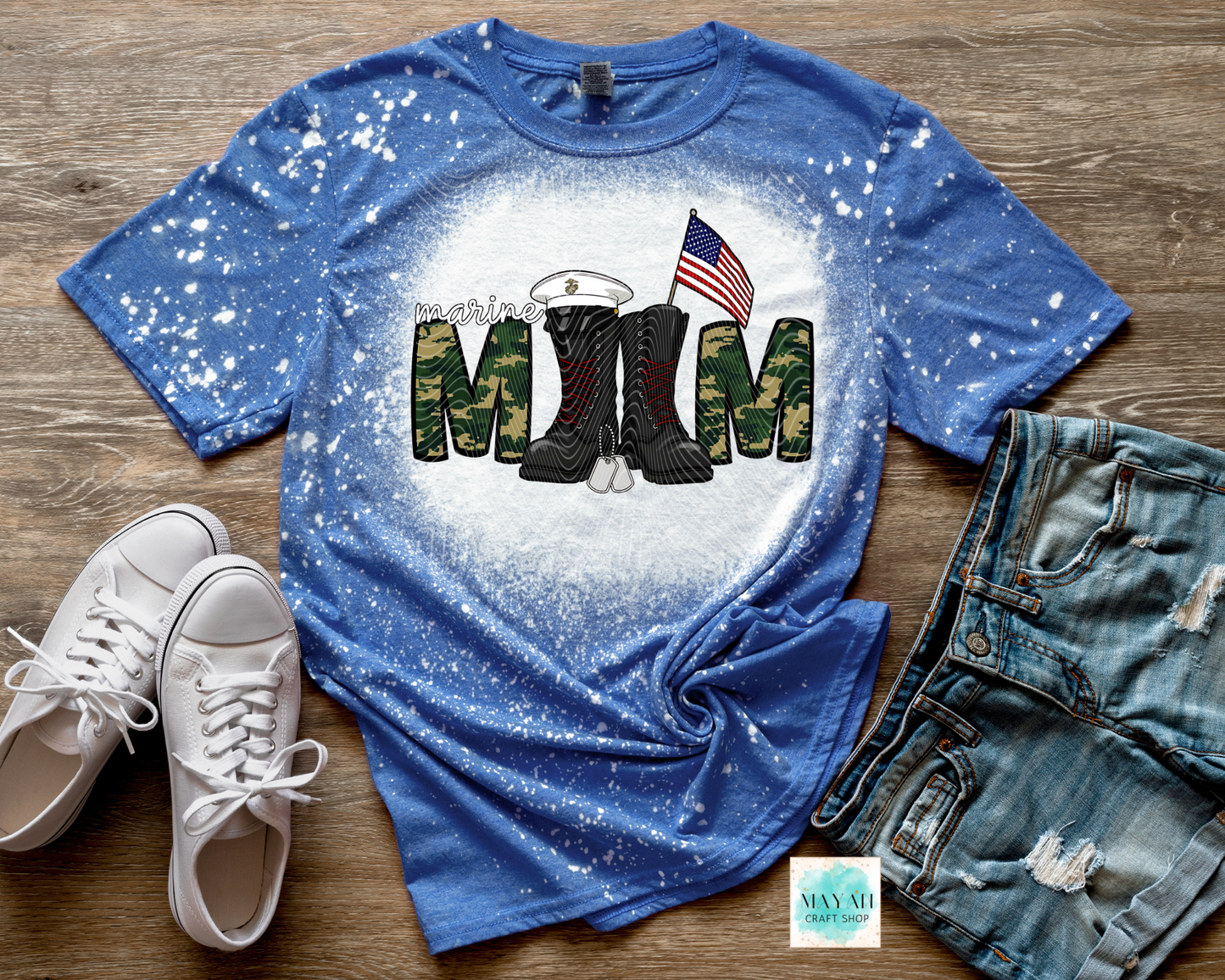 Blue t-shirt with military-themed design on a wooden surface with shoes and jeans.