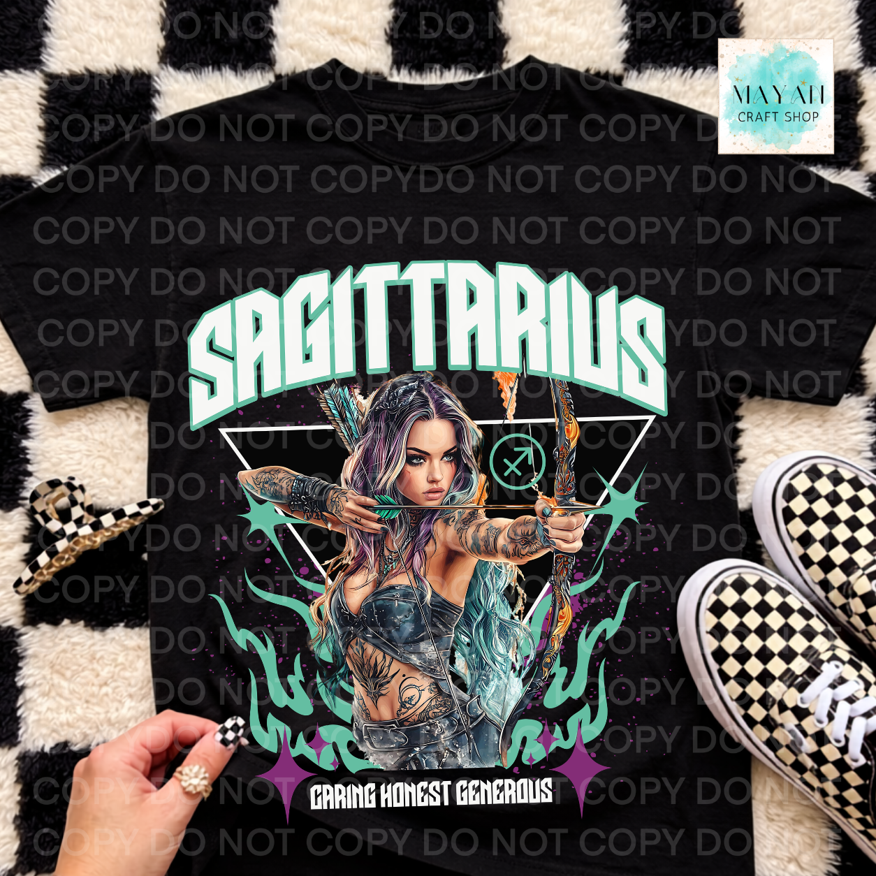 A black graphic t-shirt featuring a stylized illustration of a tattooed woman with a bow and arrow, with the text 'SAGITTARIUS' and 'CARING HONEST GENEROUS' on a black and white checkered rug, styled with sneakers and a hand holding a checkered accessory.