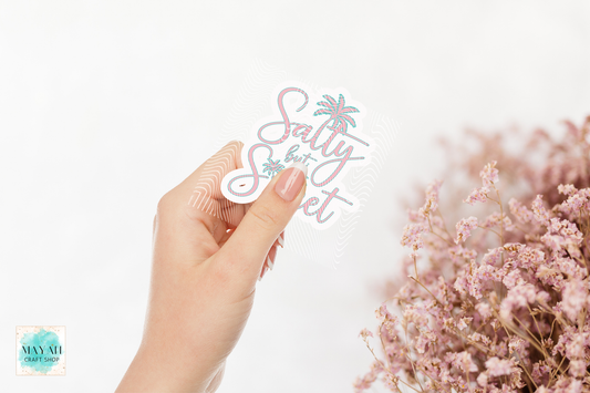Hand holding a 'Salty but sweet' sticker with pink flowers on a light background