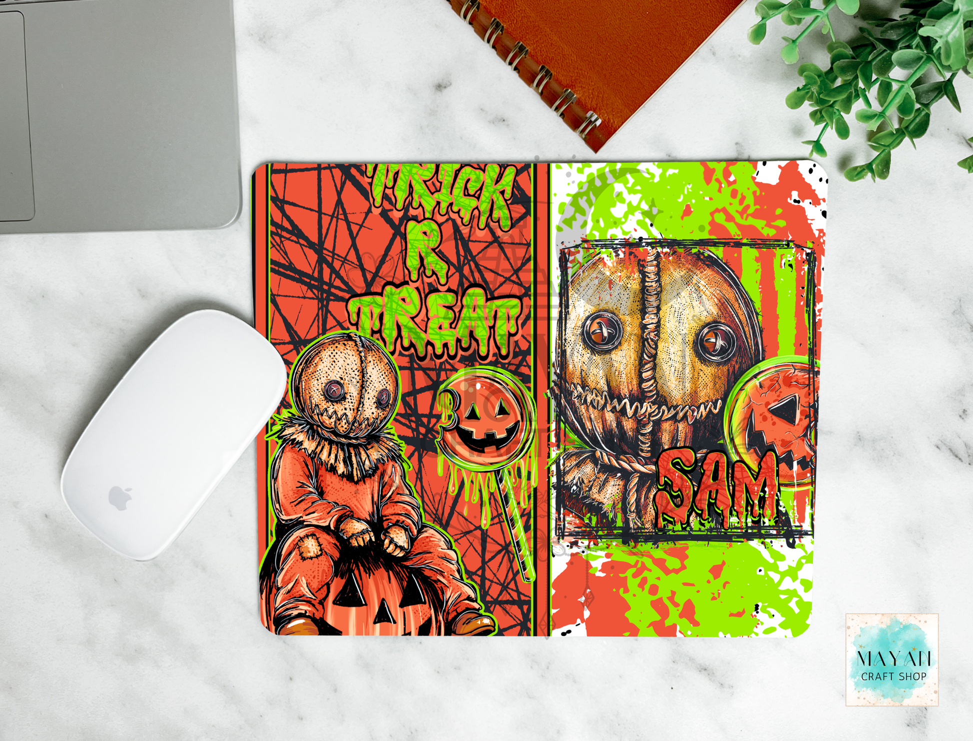 A mouse pad featuring a split Halloween design with a scarecrow on the right and Trick or Treat on the left, shown on a white marble desk with a white mouse, notebook, and plant.