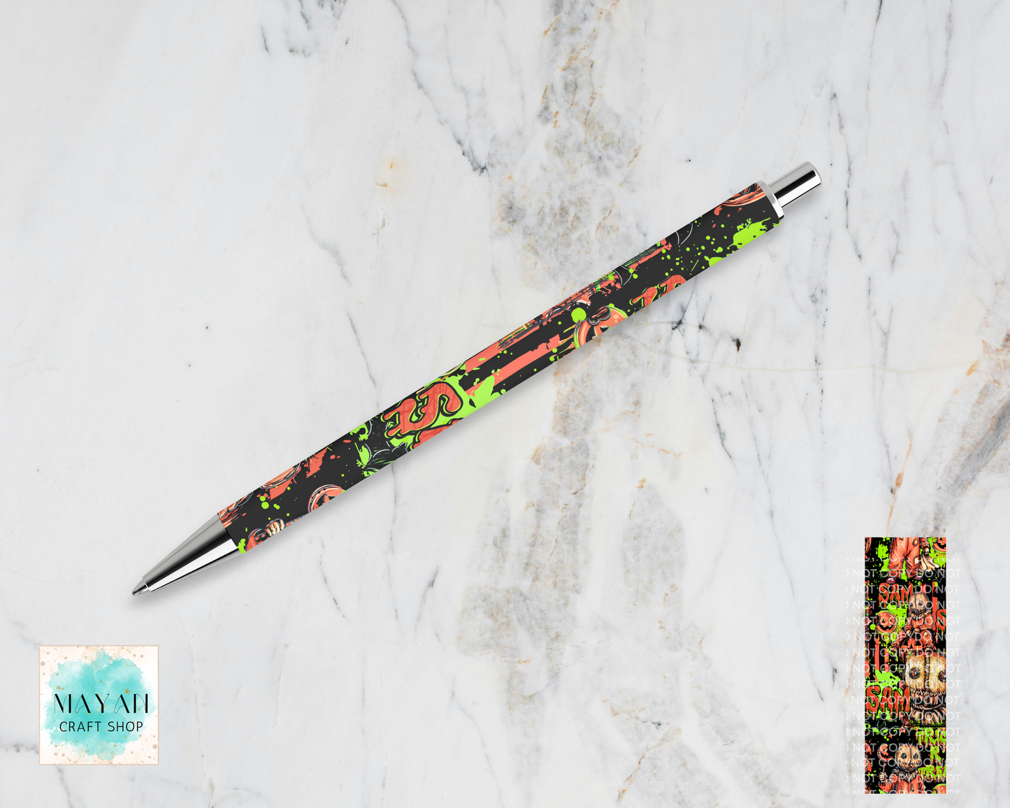 A slim ballpoint pen with a black body decorated with a colorful graffiti-style pattern of orange, green, and pink, resting diagonally on a white marble background. A small color swatch is shown in the bottom-right corner.