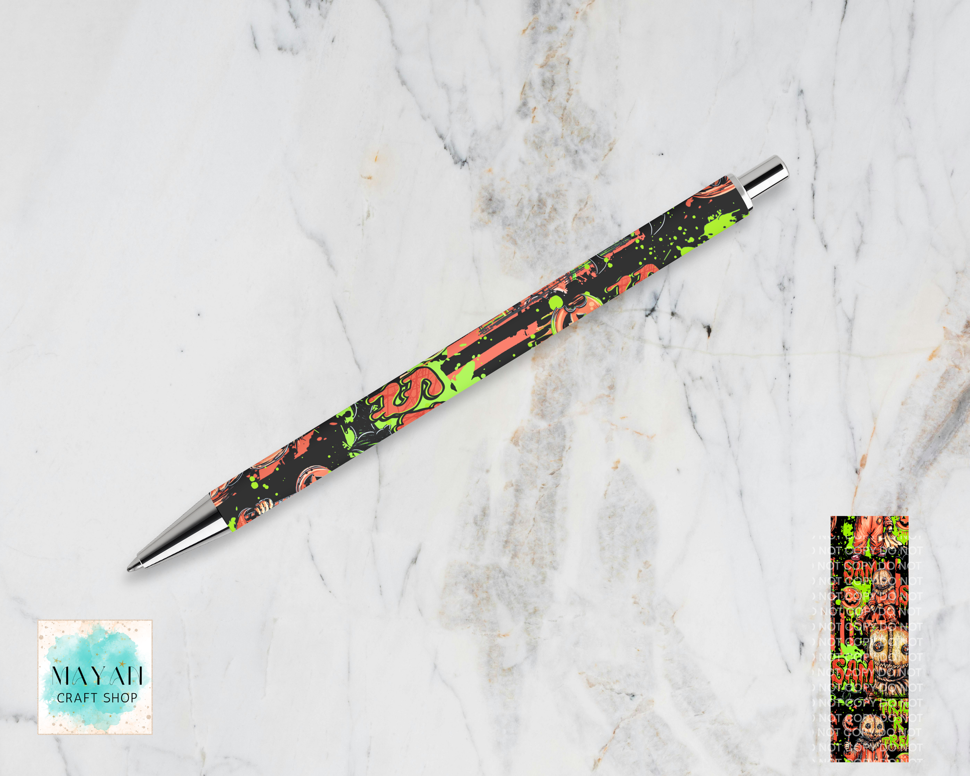 A slim ballpoint pen with a black body decorated with a colorful graffiti-style pattern of orange, green, and pink, resting diagonally on a white marble background. A small color swatch is shown in the bottom-right corner.