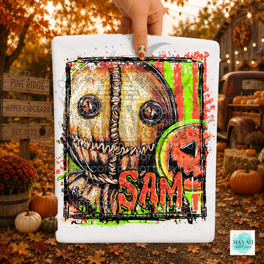 A hand holds a white shirt featuring a Halloween-style illustrated scarecrow face against an autumn outdoor scene with pumpkins, fall leaves, and rustic signs.