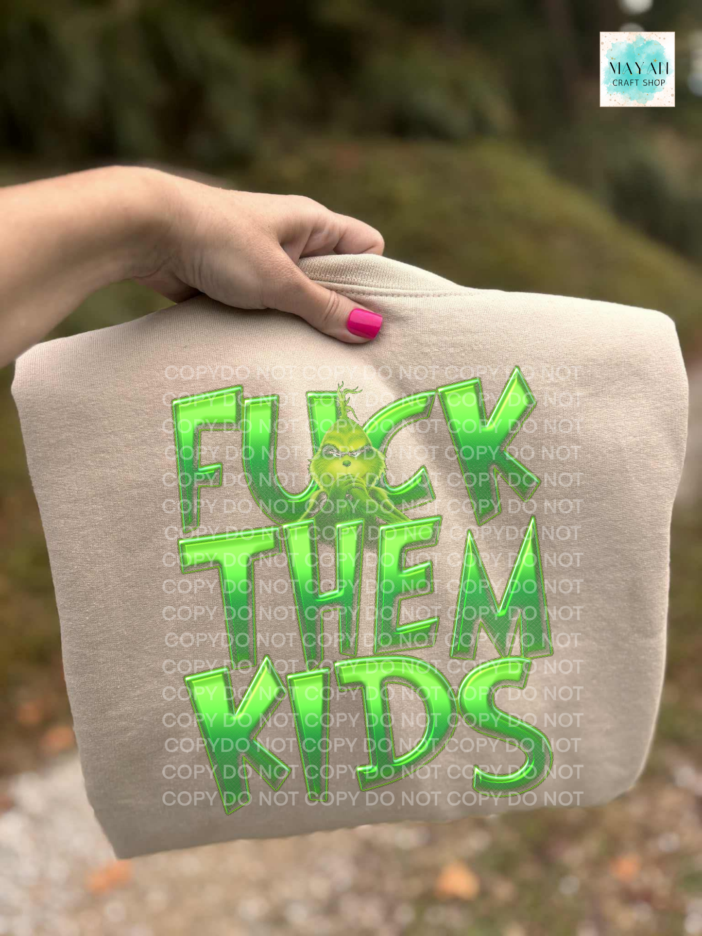 Sand sweatshirt with green text held by a hand against a blurred natural background