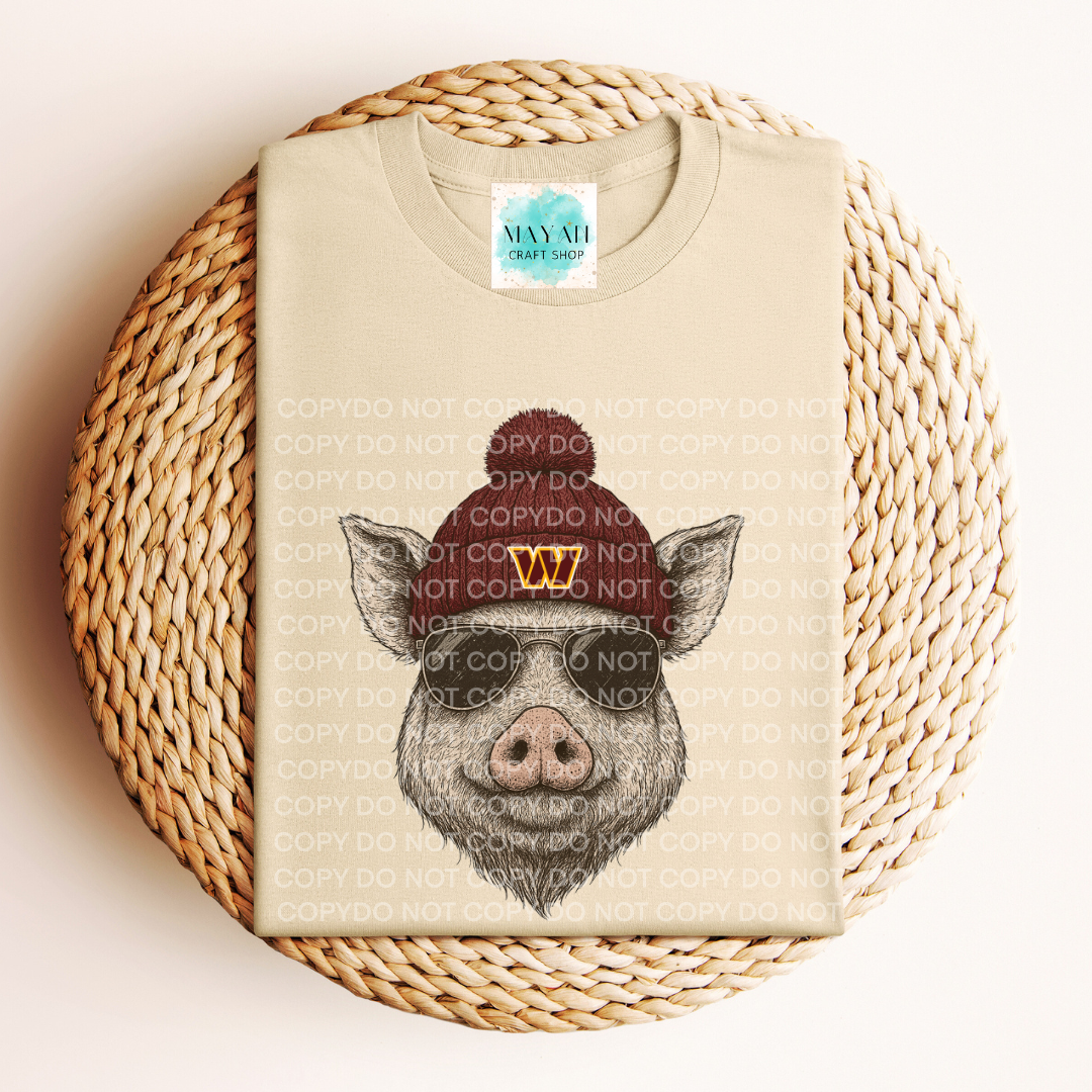 Beige t-shirt with a graphic of a pig wearing a hat on a woven mat
