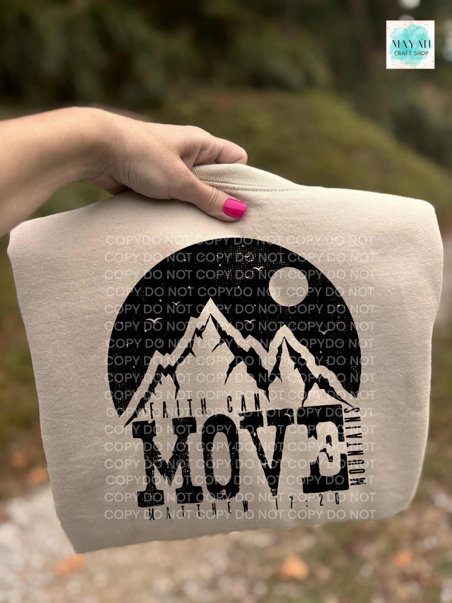 Beige sweatshirt with mountain design and 'Move' text held by a hand outdoors.