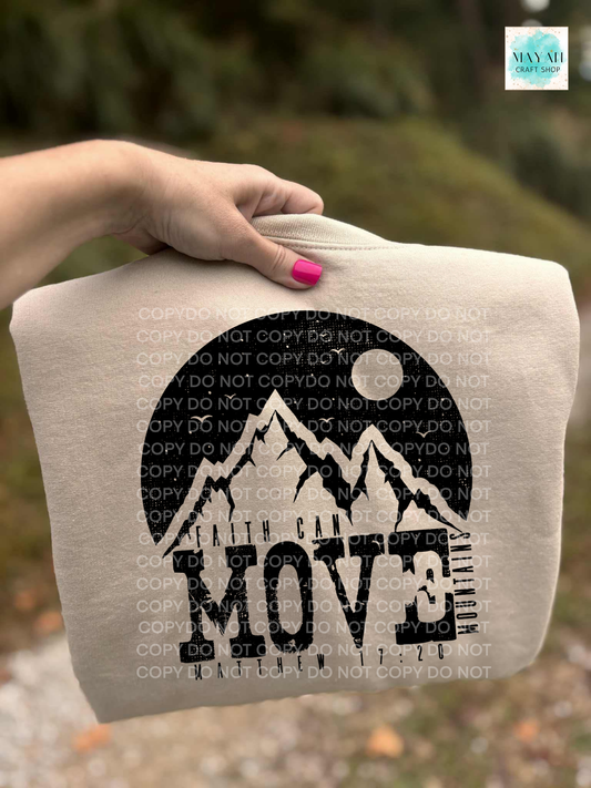 Beige sweatshirt with mountain design and 'Move' text held by a hand outdoors.