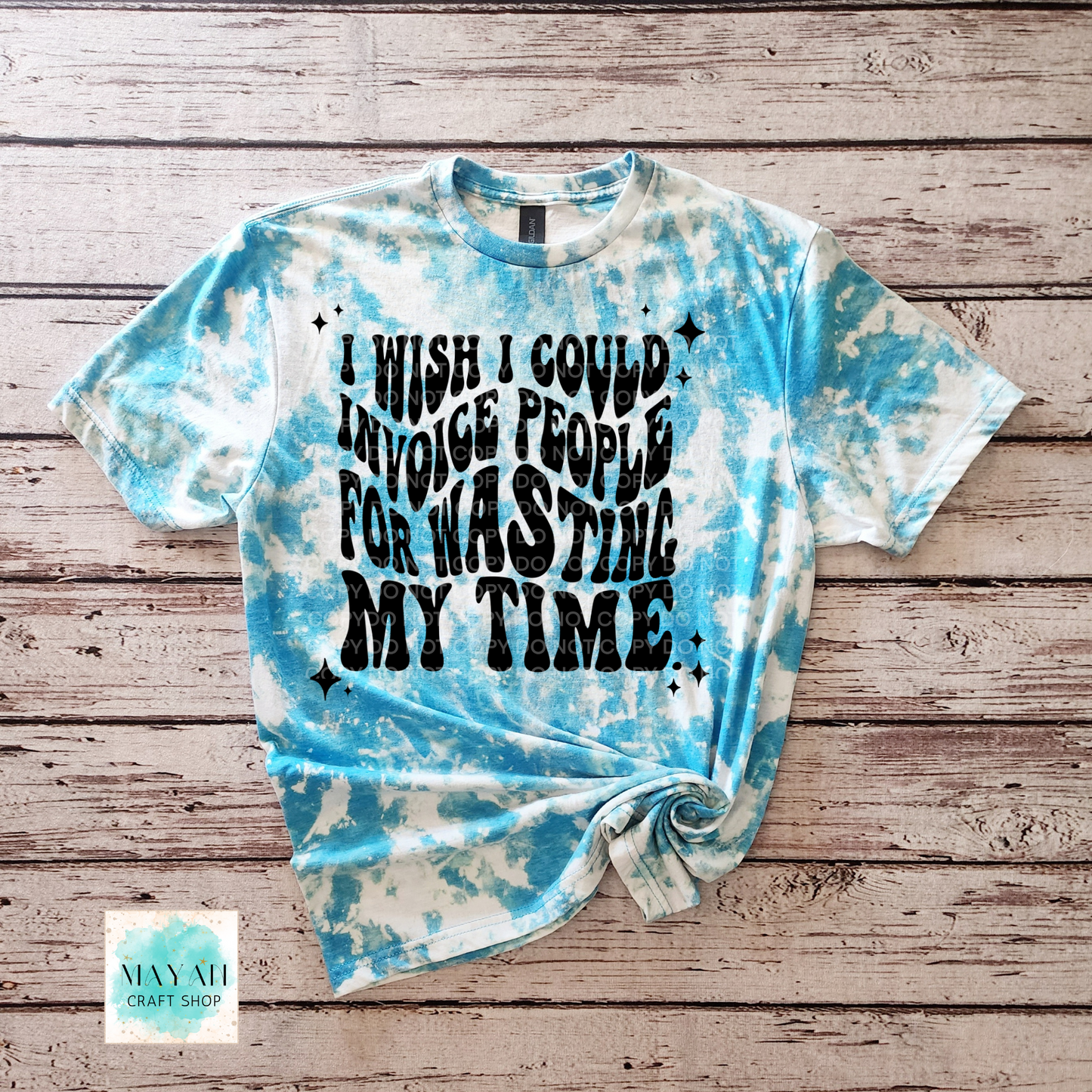 Tie-dye t-shirt with text on a wooden surface, featuring the brand 'Mayan Craft Shop'.