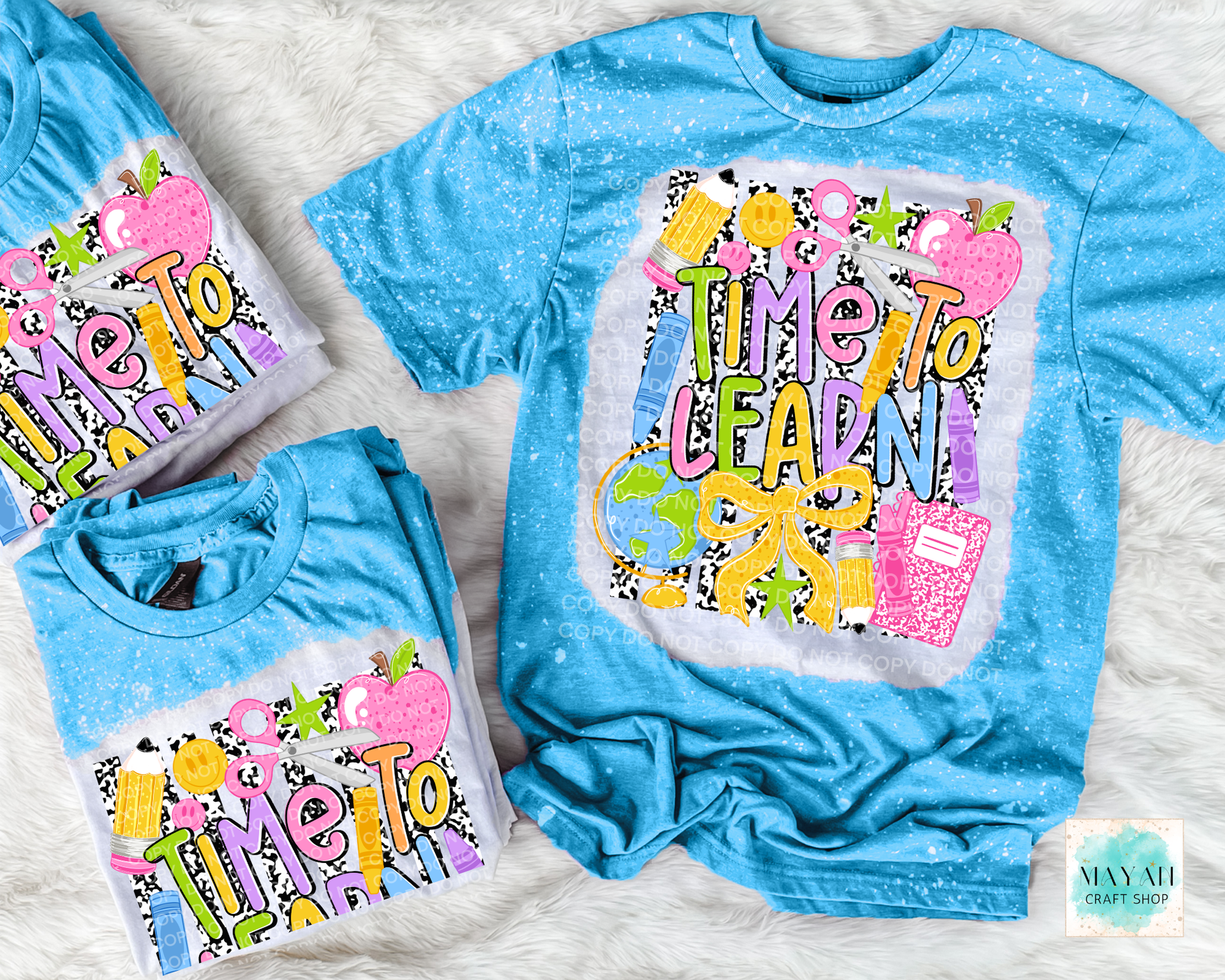 Three blue short-sleeve graphic T-shirts arranged on a white faux-fur background. The shirts feature a colorful 'Time To Learn' school-themed design with apples, pencils, and a notebook.