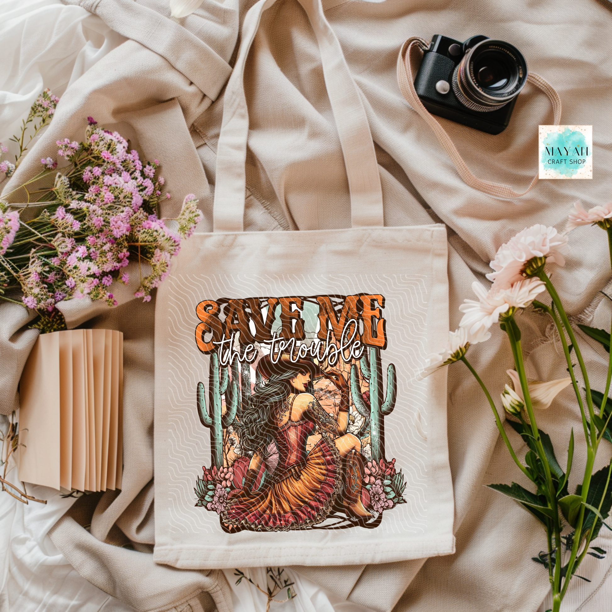 Tote bag with artistic design and text on a soft fabric background with flowers and a camera.