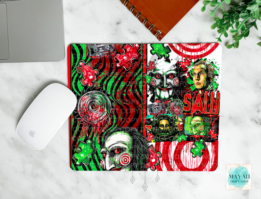 A mouse pad featuring a highly detailed, colorful horror-themed collage design inspired by a horror movie, styled in a flat-lay on a white marble surface next to a white computer mouse and an orange spiral notebook.