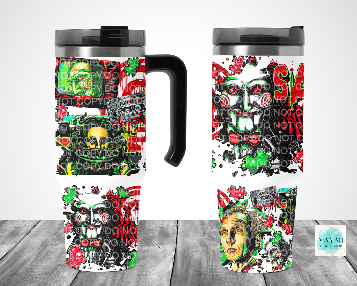 Two insulated travel mugs with black lids and handles, shown from front and side views on a gray wood surface. The mugs feature a bold horror-themed collage print with faces, cassette tapes, and graffiti-style graphics in red, green, black, and white.