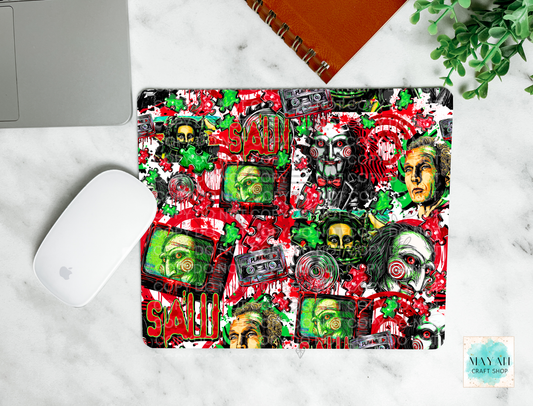 A mouse pad with a vibrant, multicolored collage print featuring the  red blood, cassette tapes, skulls, and faces, shown in a flat-lay setup on a white marble desk alongside a laptop, mouse, notebook, and plant.
