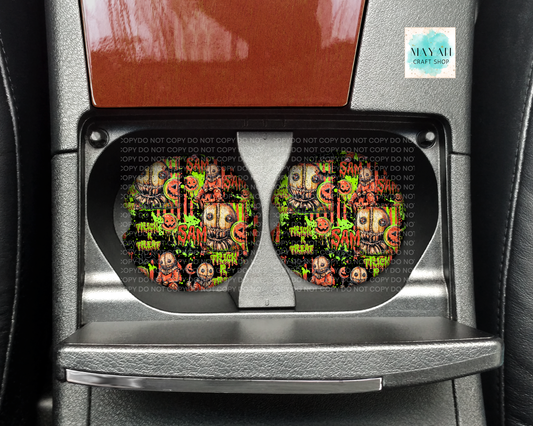 A pair of Halloween-themed car cup holders installed in a center console. The cup holders feature a colorful graphic print with skulls, ghosts, and words on a black background.