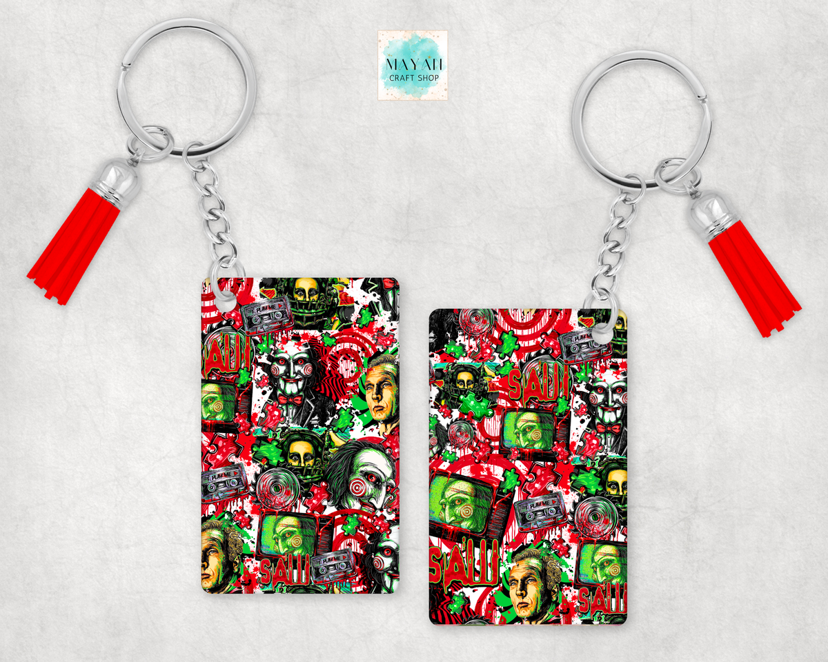 Two keychains with red tassels, featuring a busy collage print of horror movie faces, skulls, and a word on a light gray textured background.
