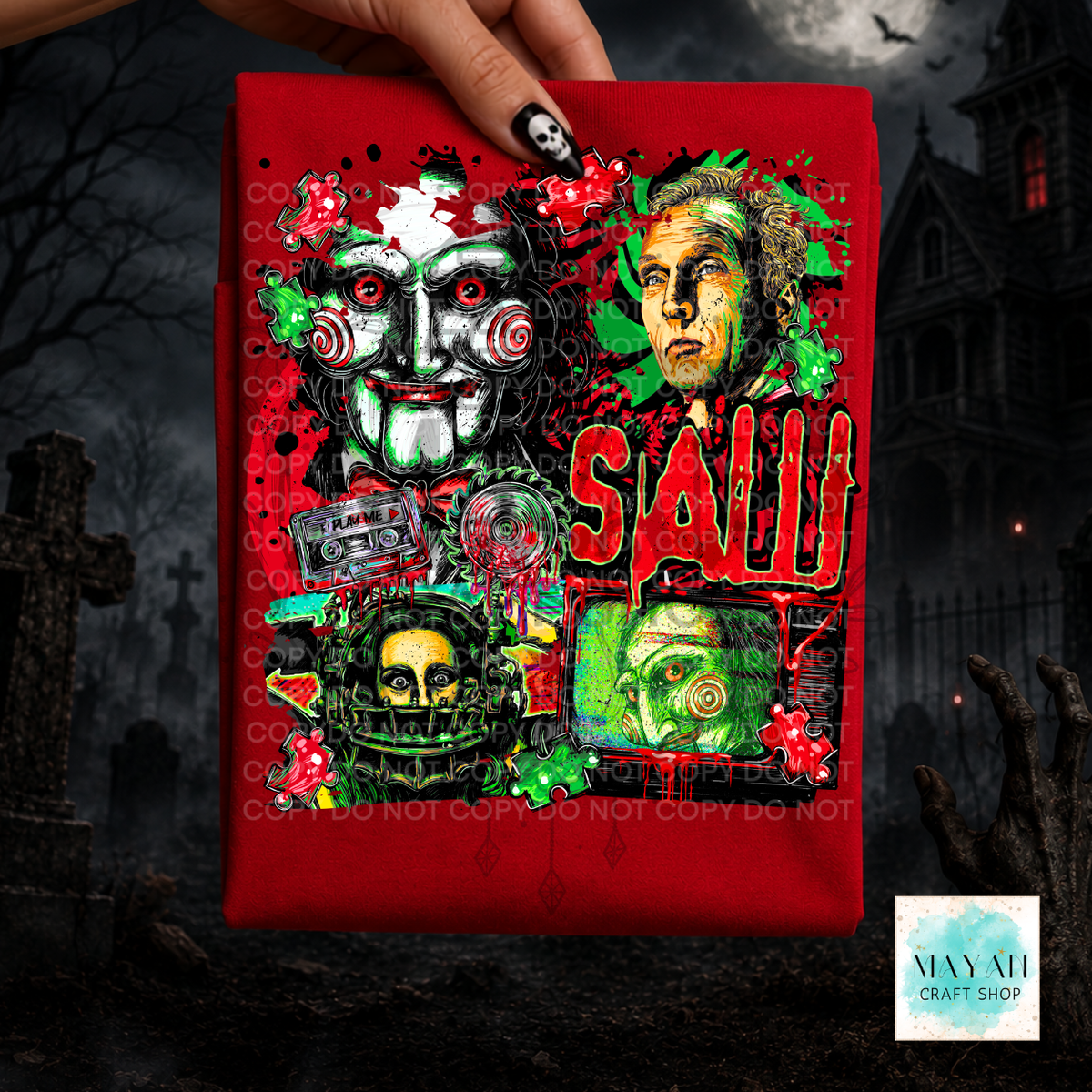 A hand holds a red rectangular fabric or print featuring a highly detailed horror graphic with multiple faces, green leaves, red splatters, in large red letters. The background is a dark, spooky graveyard scene with tombstones and a haunted house.