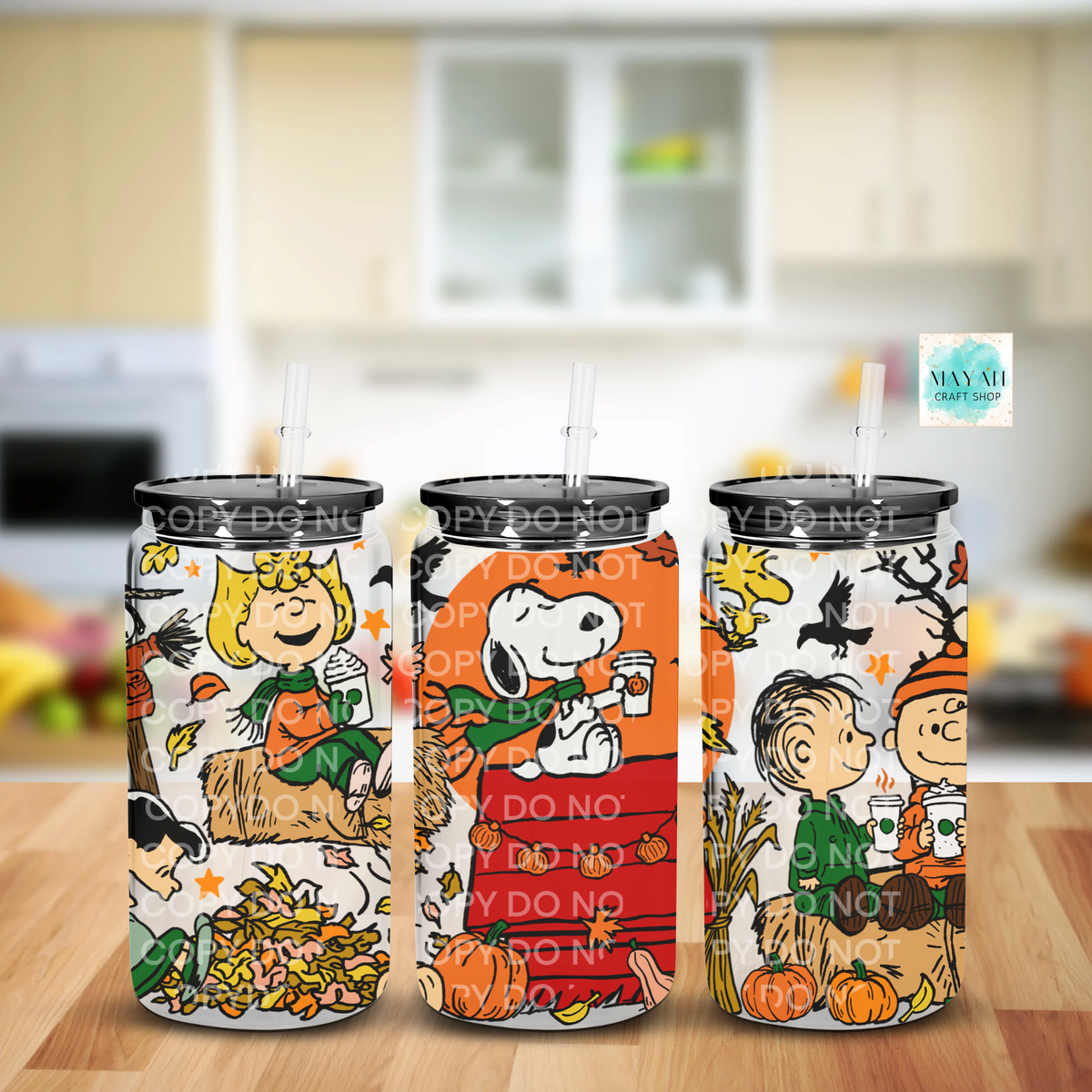 Three frosted glass cans with black lids and clear straws, printed with autumn-themed cartoon scenes and characters. The glass cans are shown on a wooden surface with a blurred kitchen background.