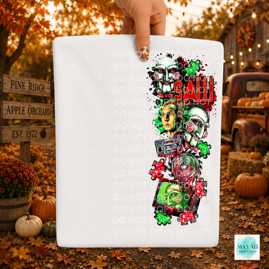 A hand holds a white rectangular fabric item, likely a bandana or small flag, featuring a colorful graphic print of horror-themed skulls, a cassette tape, puzzle pieces. The background is a blurred autumn outdoor scene with pumpkins, fall leaves, and a rustic truck.