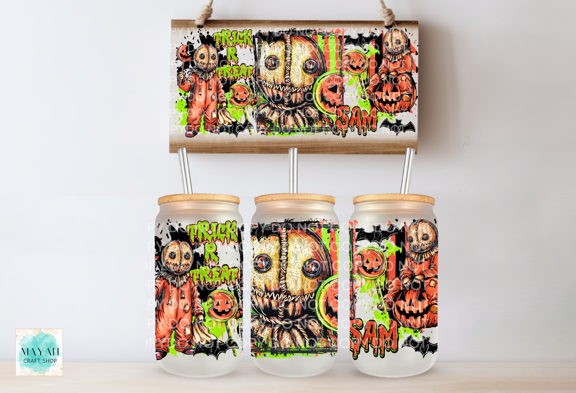 Three frosted glass mason jars with bamboo lids and metal straws, decorated with a spooky Halloween graphic featuring a stitched scarecrow, pumpkins.
