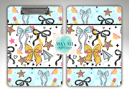 Two matching clipboard-style art boards with a repeating craft-themed pattern of bows, stars, pencils, hearts, and small geometric shapes on a light blue background. 