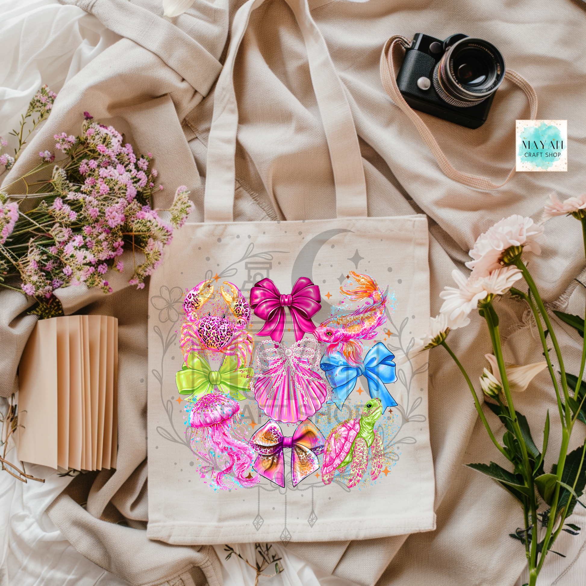Tote bag with colorful bow design on a light fabric background with flowers and a camera.