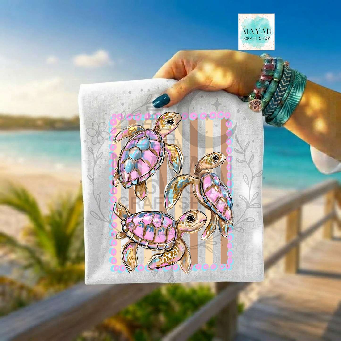 Hand holding a shirt with turtle designs against a beach background