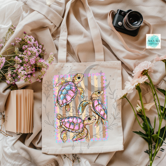 Tote bag with colorful turtle design on a soft fabric background with flowers and a camera.