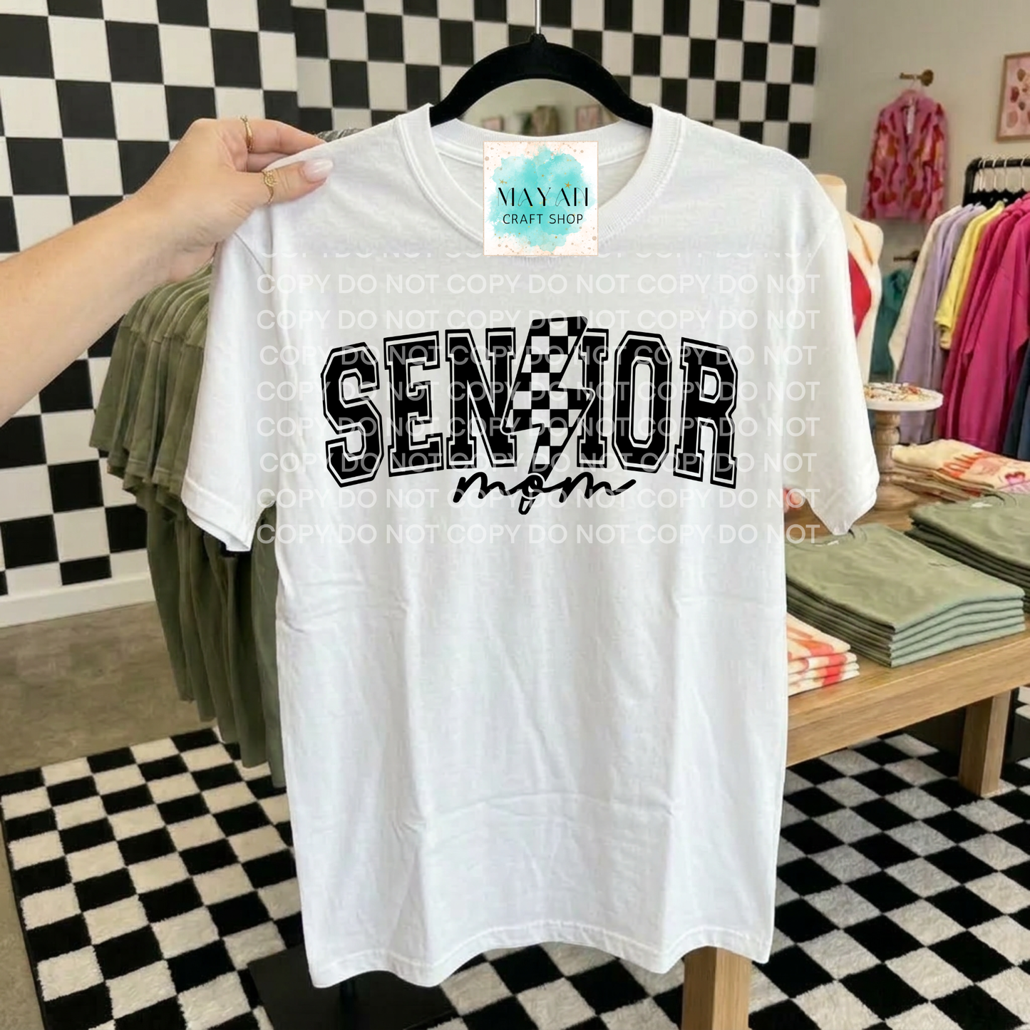 White t-shirt with 'SENIOR mom' text held up against a checkered floor background.