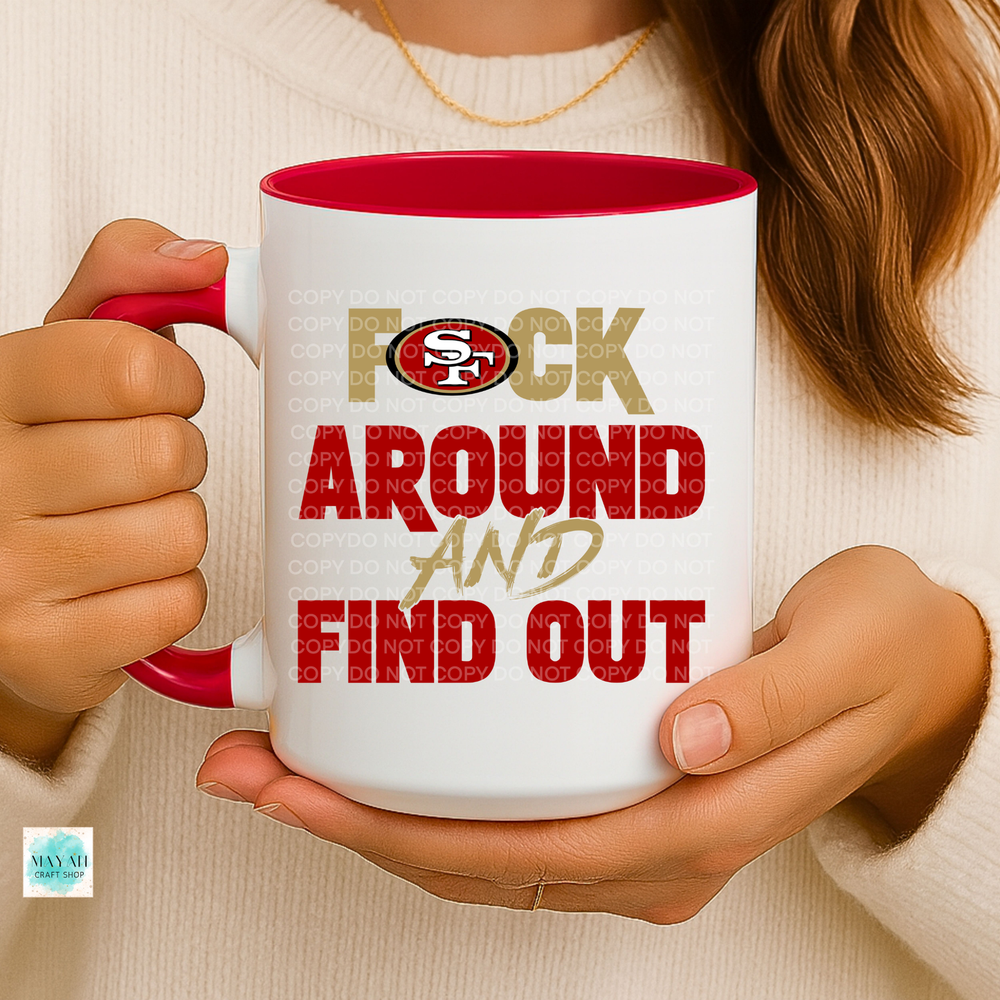 Person holding a mug with text and a logo, wearing a beige sweater.