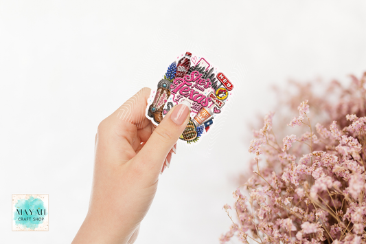 Hand holding a colorful sticker with text, surrounded by pink flowers on a light background.