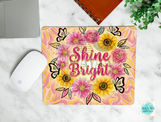 Mouse pad with floral design and 'Shine Bright' text on a marble surface.