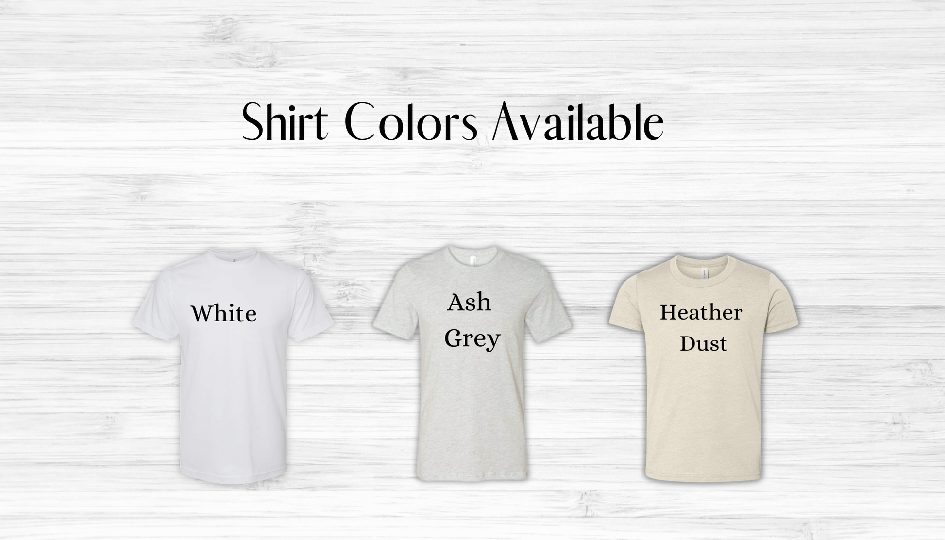 Three short-sleeve crew-neck T-shirts displayed on a light wood background with the text 'Shirt Colors Available' above them. The shirts are labeled 'White', 'Ash Grey', and 'Heather Dust' in black text on the chest.