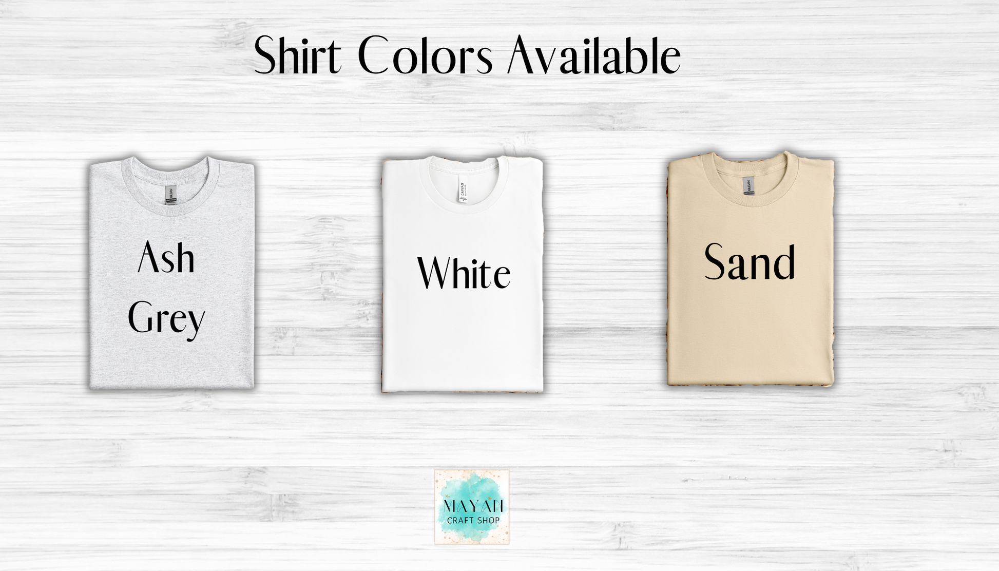 Three t-shirts in ash grey, white, and sand with text labels on a light wooden background.