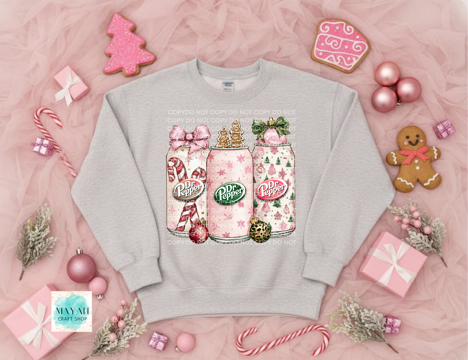 Gray sweatshirt with soft drink holiday design surrounded by Christmas-themed decorations on a pink background