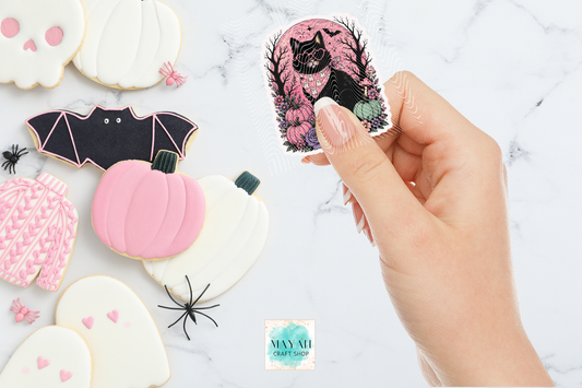 Sticker shaped like a black cat, pink pumpkin, and bat with a hand holding a similar cookie design.