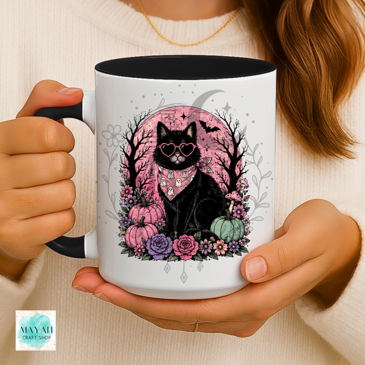 Person holding a mug with a black cat design featuring flowers and pumpkins.