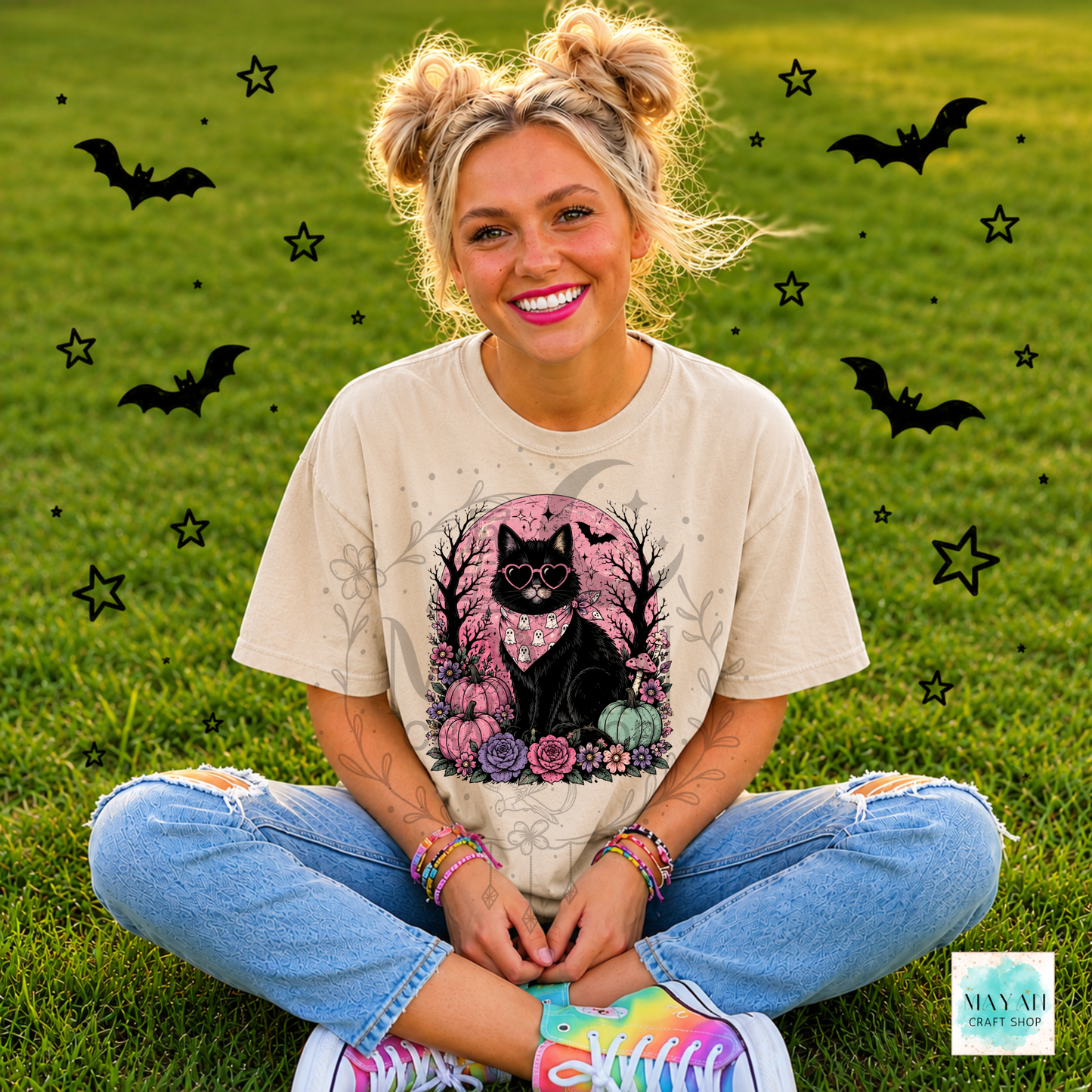 Person sitting on grass with Halloween-themed decorations, wearing a t-shirt with a black cat design.